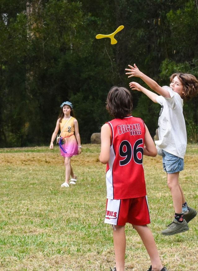 Children playing with a yellow boomerang in a grassy field.