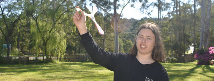 Person holding a white Superang boomerang outdoors with trees and grass in the background