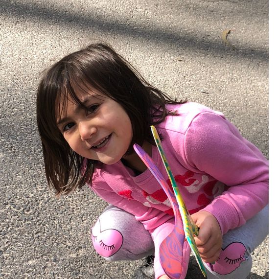 Child in pink outfit holding a colorful boomerangs on a concrete surface